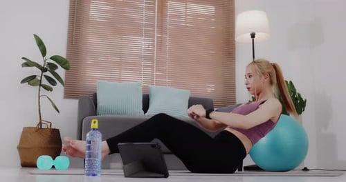 Young Asian woman in sportswear doing exercise and watching fitness tutorial online video on tablet.