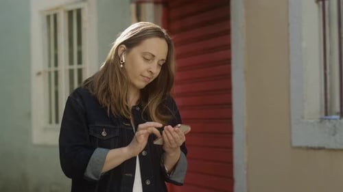 Smiling brunette woman uses her phone in the city. Pretty woman looking at her mobile phone