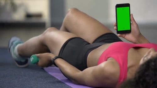 Mixed Race Young Female Using Phone with Green Screen, Flexing Arm with Dumbbell