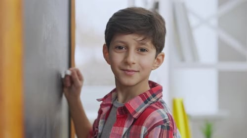 Smiling Boy Writing on Chalkboard in Classroom