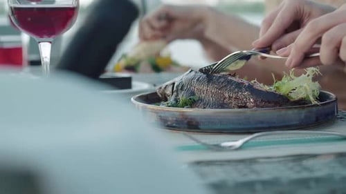 Side View Close-up of Female Hands Cutting Fried Fish on Plate. Unrecognizable Woman Eating Tasty