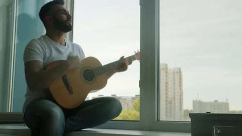 Man Plays Guitar and Sings by Apartment Window