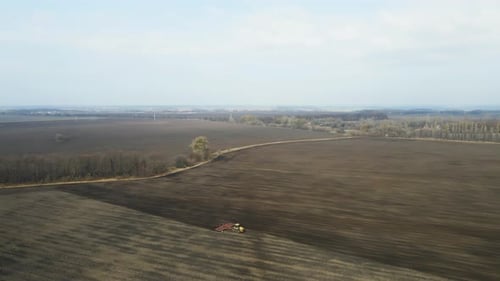 Aerial view of a modern yellow tractor plowing dry agricultural field , preparing land for sowing
