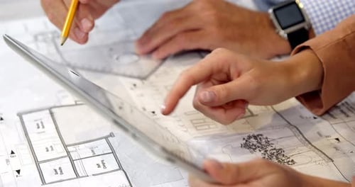 Geschäftsfrau nutzt digitales Tablet, während Kollegin an Blueprint arbeitet