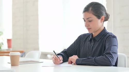 Woman Writes on Paper at Desk in Office