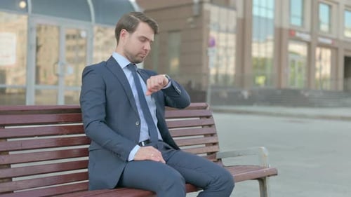 Empresário verificando o tempo enquanto espera no banco ao ar livre