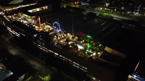 Night, aerial and circular view of a shopping center with an amusement park with colored lights on t