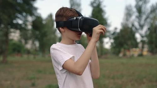 Happy Boy in Virtual Reality Glasses Plays Video Games Outdoors