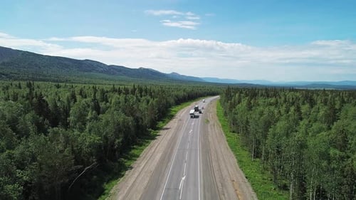 Luftaufnahme eines Intercity-Highway mit Verkehr durch einen grünen Wald an einem hellen, sonnigen Tag