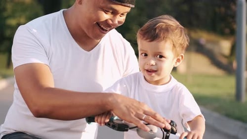 Dad Teaching Son To Drive a Bike in the Summer Park