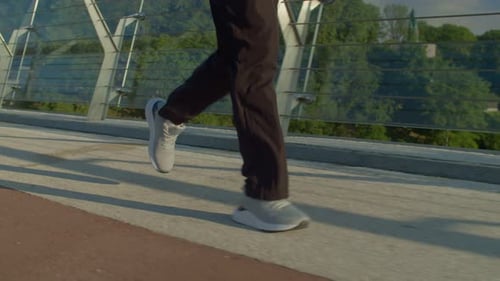 Closeup of Male Legs in Sports Shoes Jogging on Bridge at Sunrise