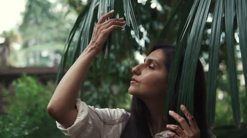 Portrait of a Woman Who Passes Her Hand Over a Leaf From a Palm Tree in the Park