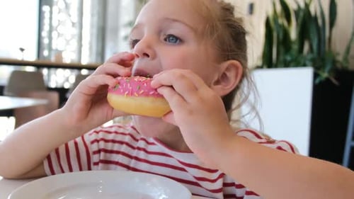 Young Girl Enjoys Eating a Pink Sprinkled Donut