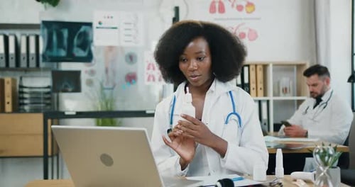 Doctora sentada frente a una computadora portátil durante una videollamada y explicando