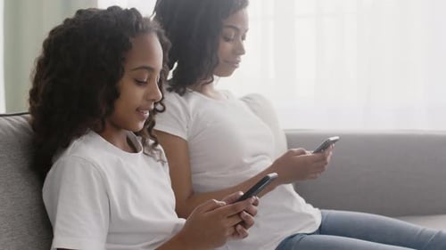 Child and Adult Using Smartphones on Sofa