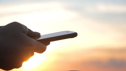 Hands Holding Smartphone at Sunset