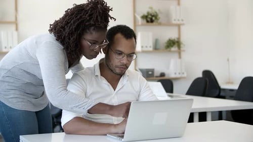 Coworkers Collaborate on Laptop at Desk in Bright Office
