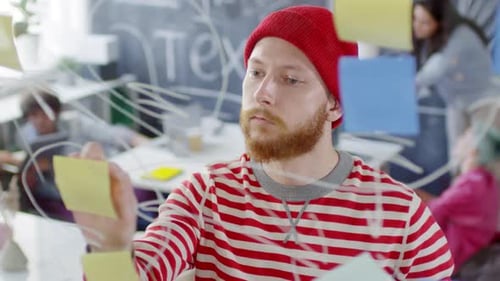 Kreativer Hipster-Mann plant Aufgaben an einer Glaswand im Büro