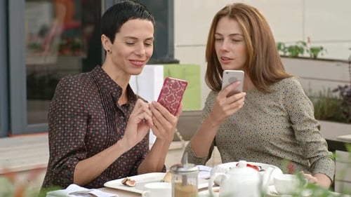 Two Women Using Phones at an Outdoor Cafe