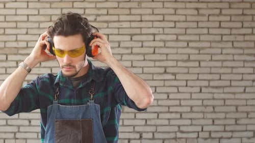 Portrait of a Young Man in a Carpenter's Workshop in Protective Glasses Looking at Camera