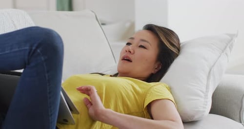 Woman Relaxes on Sofa with Laptop and Tablet