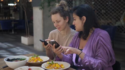 Two Women Friends Using Phone at Outdoor Cafe