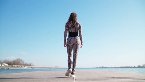 Young Slim Girl in Sportswear Is on the Pier Along the Lake