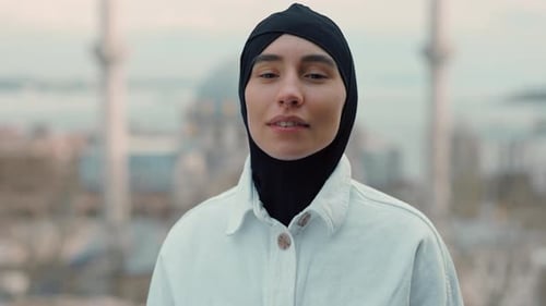 Porträt einer schönen muslimischen Frau, die im schwarzen Hijab in die Kamera blickt, auf dem Hintergrund des