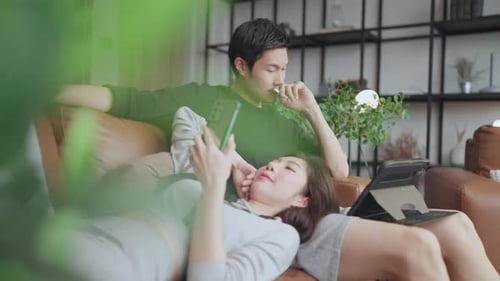 Young Couple Relaxing with Technology on Couch Indoors