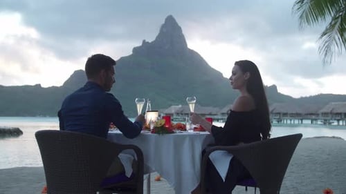 Man and woman couple toasting with champagne on beach, tropical island resort sunset, Bora Bora