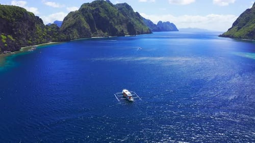 Aerial Drone View of White Traditional Filipino Boat Floating on Top of Clear Blue Water Surface