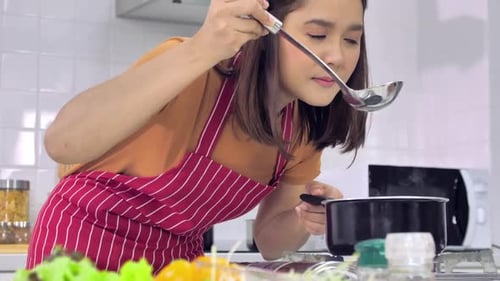 Woman Cooking and Tasting Food in Kitchen