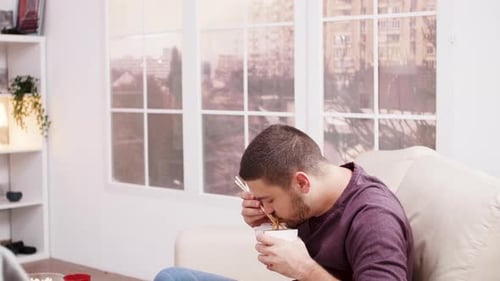 Man Enjoys Eating Noodles on the Sofa
