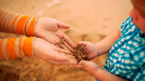 Child Receives Sand from Parent at Beach