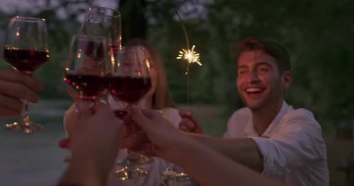 Youth Friendship Concept Hands Toasting Red Wine Glass Beside River at Nightime