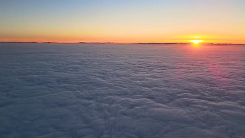 Aerial View of Colorful Sunset Over White Dense Foggy Clouds Cover with Distant Dark Silhouettes of