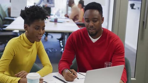 African american male and female business colleagues talking and using laptop in office