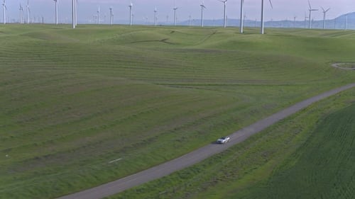 Car Driving On The Dirt Road Among Windmills