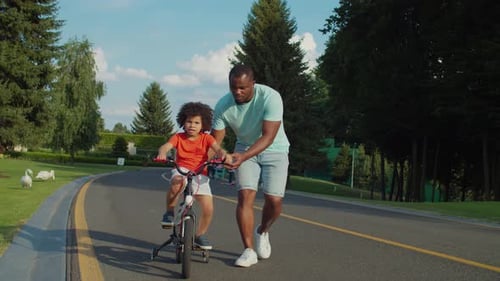 Loving Father Teaching Son To Ride Bicycle in Park
