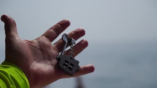 Keys with a Houseshaped Keychain in a Man's Hand on Sea Beach Background