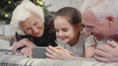 Girl Using Tablet with Grandparents Near Christmas Tree