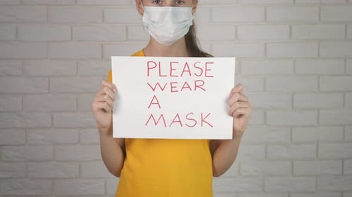 Child Wearing Mask Holds Sign