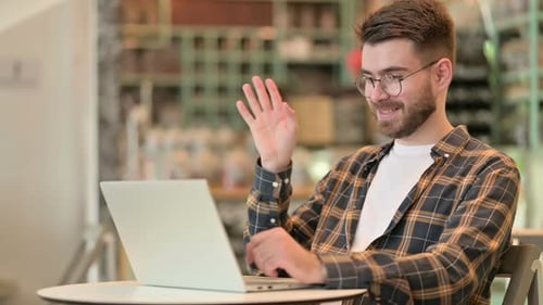Young Man Doing Video Call on Laptop in Cafe