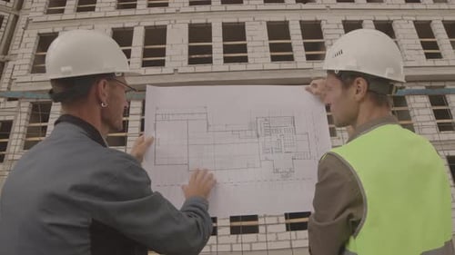 Workmen Holding Blueprint by Construction in Progress