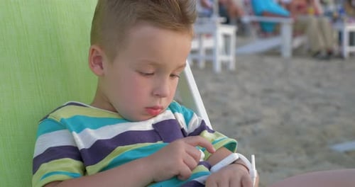 Boy Uses Smart Watch While Sitting on Beach