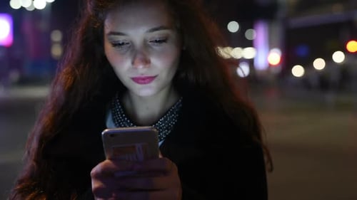 Young Woman Using Smartphone at Night in City