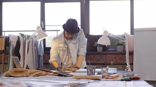 Male Fashion Designer Drawing at Worktable in Sewing Studio