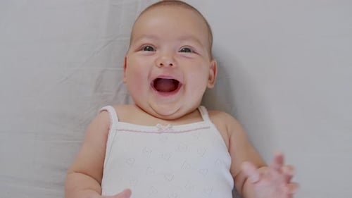 A Nice Little Caucasian Newborn Baby Is Funny Smiling, Lying at the Back in the Child Crib. Portrait