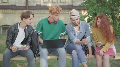 Positive Confident Man Showing Smartphone Screen To Groupmates Outdoors. Four Caucasian University