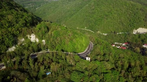 Aerial View of a Curved Winding Road Trough the Mountains with Green Trees